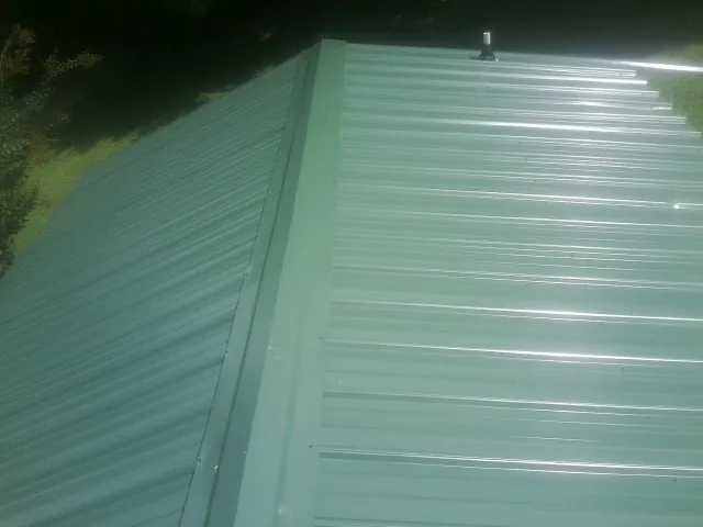 New green metal panels meeting at the ridge of a roof — Flat Roof Repair work by our crew in Gates
